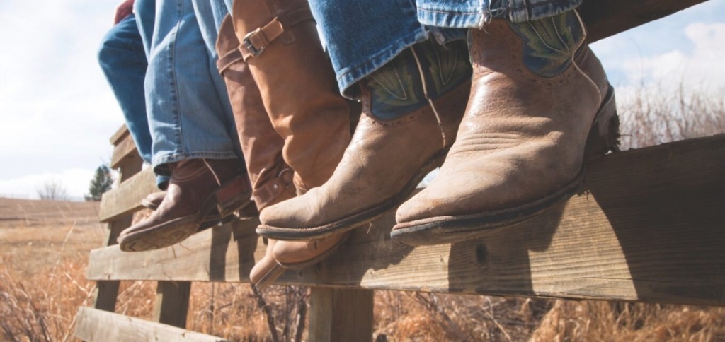 cowboys and cowgirls sitting on wooden fence prove that are wearing Ariat boots